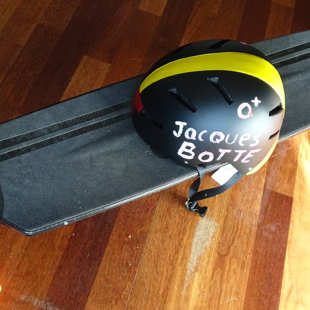 A longboard next to a helmet hand-painted with the name Jacques Botte.